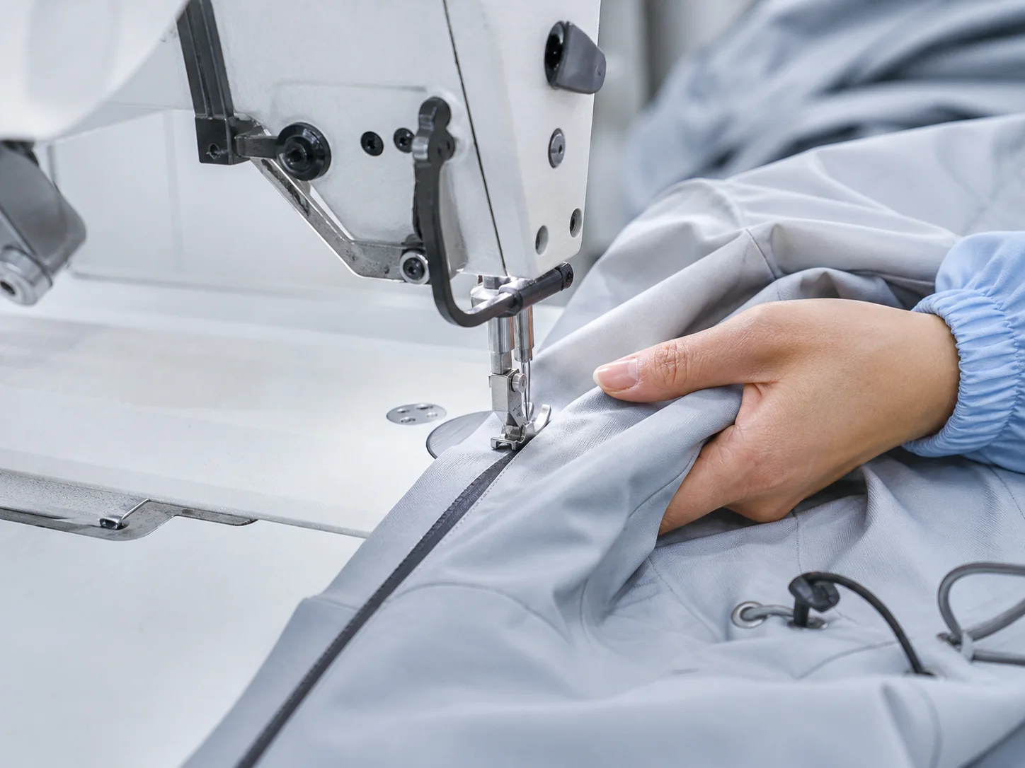 Industrial sewing machine stitching a waterproof jacket sleeve